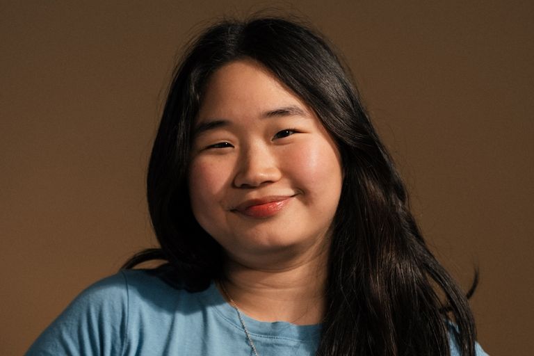 Close-up studio portrait of Danielle Lim wearing a blue top against a warm beige background, shot by Ben Raschella.